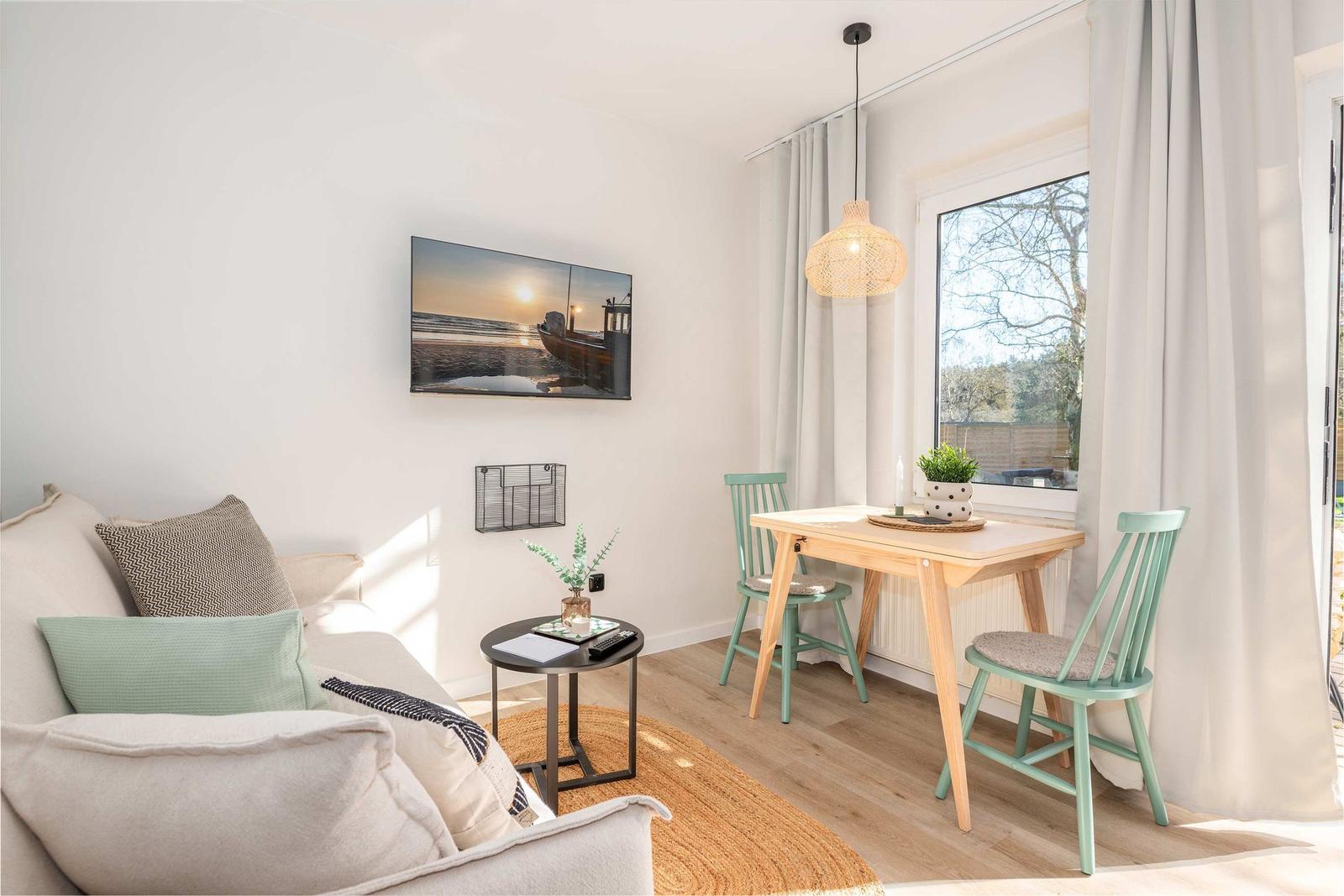 Wohnbereich mit Sofa, Esstisch und Fenster. Wandbild und Beleuchtung sichtbar.