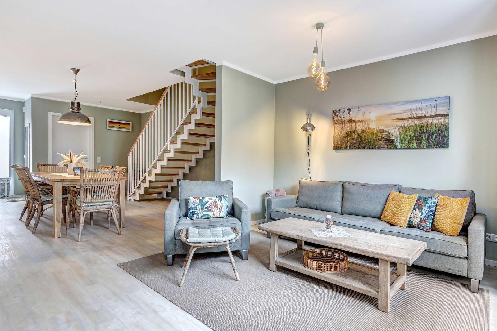 Wohn- und Essbereich mit Sofa, Stuhl und Tisch. Hintergrund: Treppe und Wandbild.