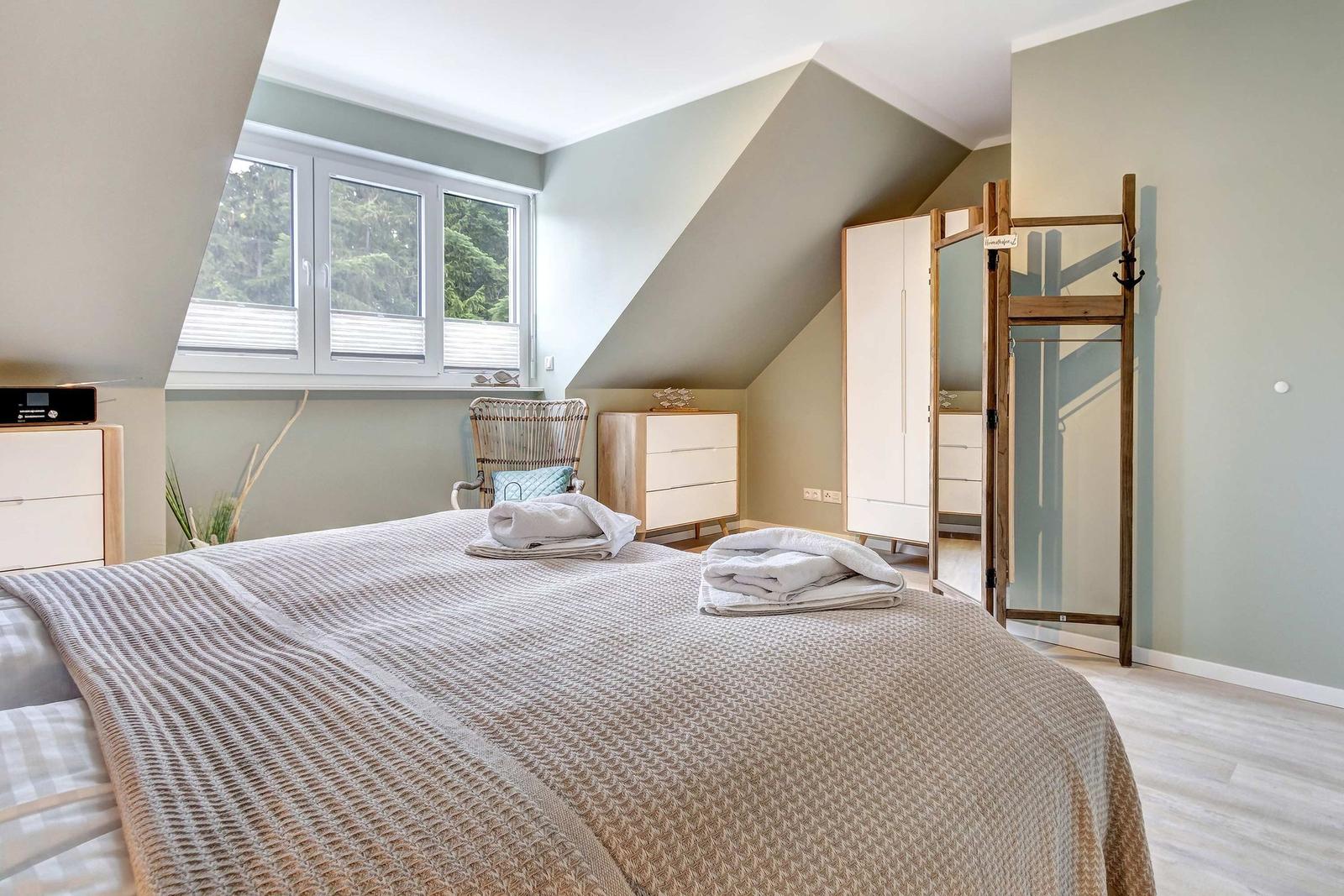 Schlafzimmer mit Dachschrägen, Fenster, Bett und Kleiderschrank.