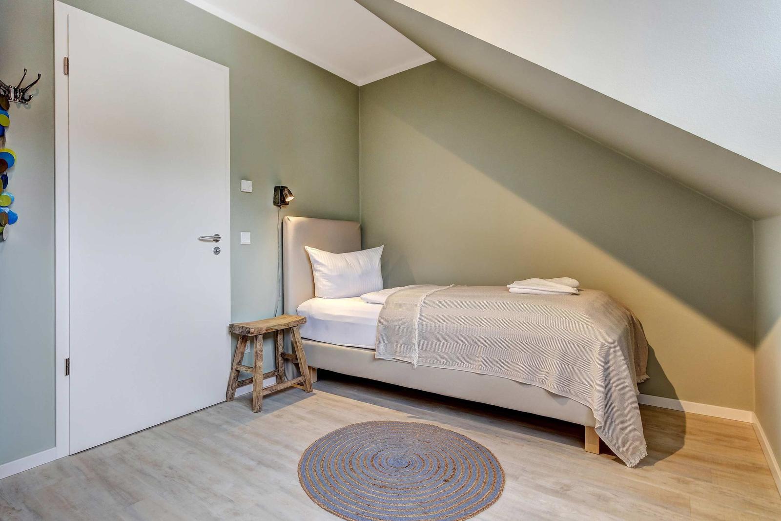 Schlafzimmer mit Dachschrägen, Bett, Stuhl und Rundteppich.