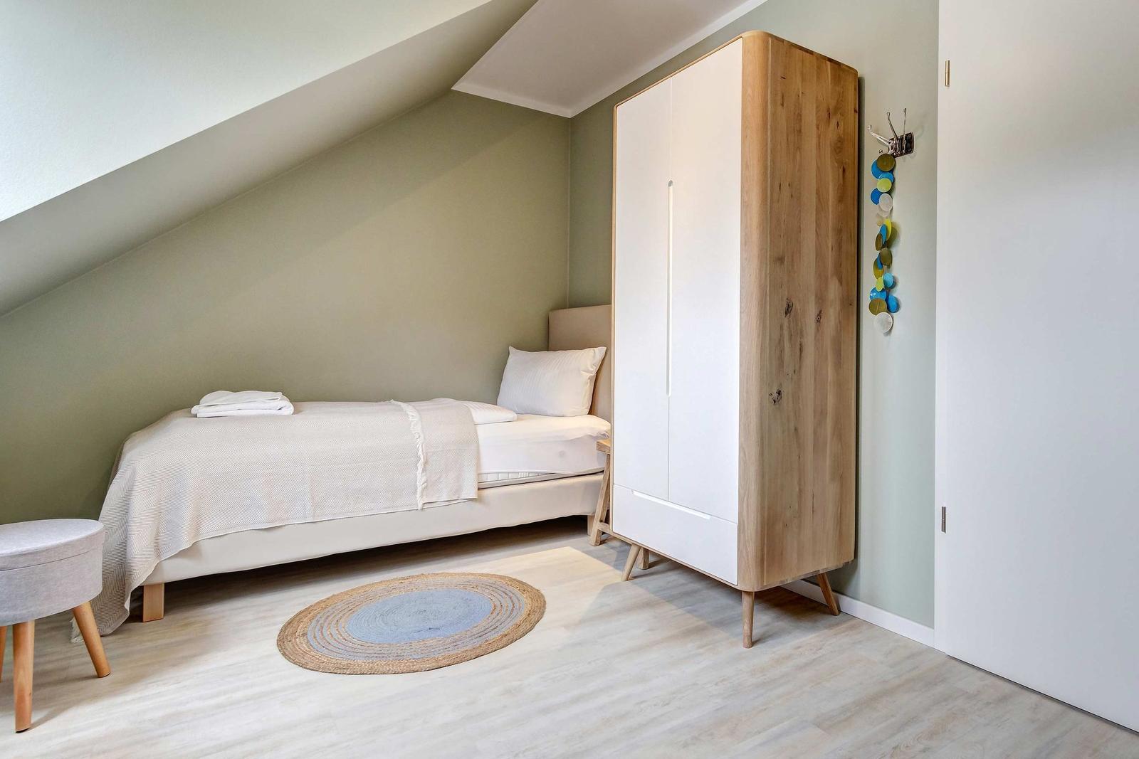 Ein Schlafzimmer mit Dachschrägen, Bett, Kleiderschrank und runden Teppich.
