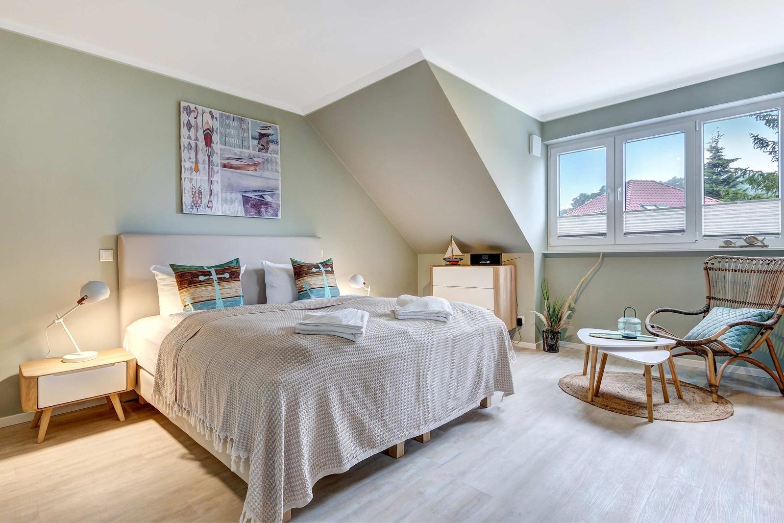 Schlafzimmer mit Dachschrägen, Bett, Nachttisch, Stuhl und Fenster mit Blick.