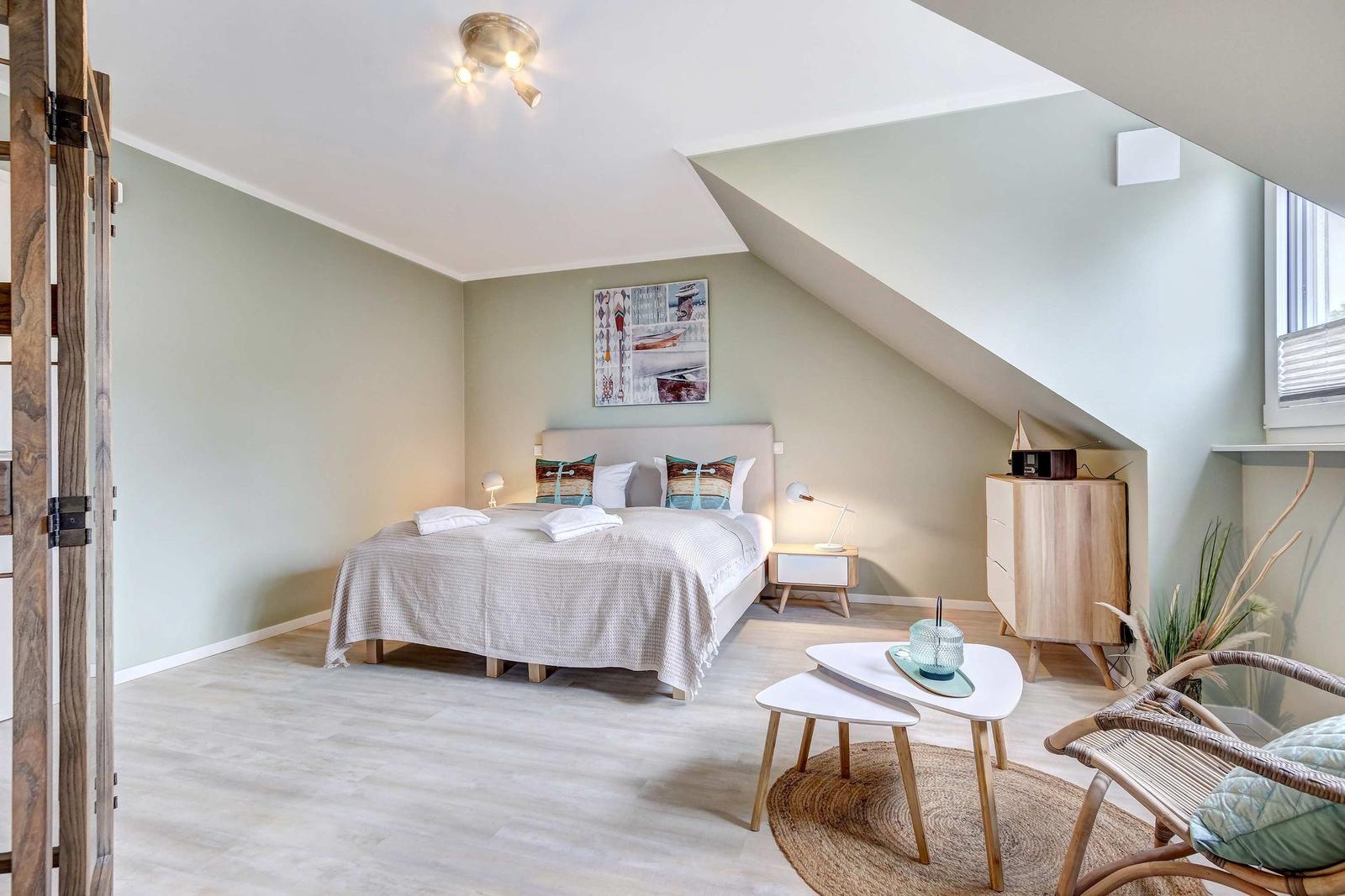 Schlafzimmer mit Dachschrägen, Bett, Nachttisch und Sitzgruppe.