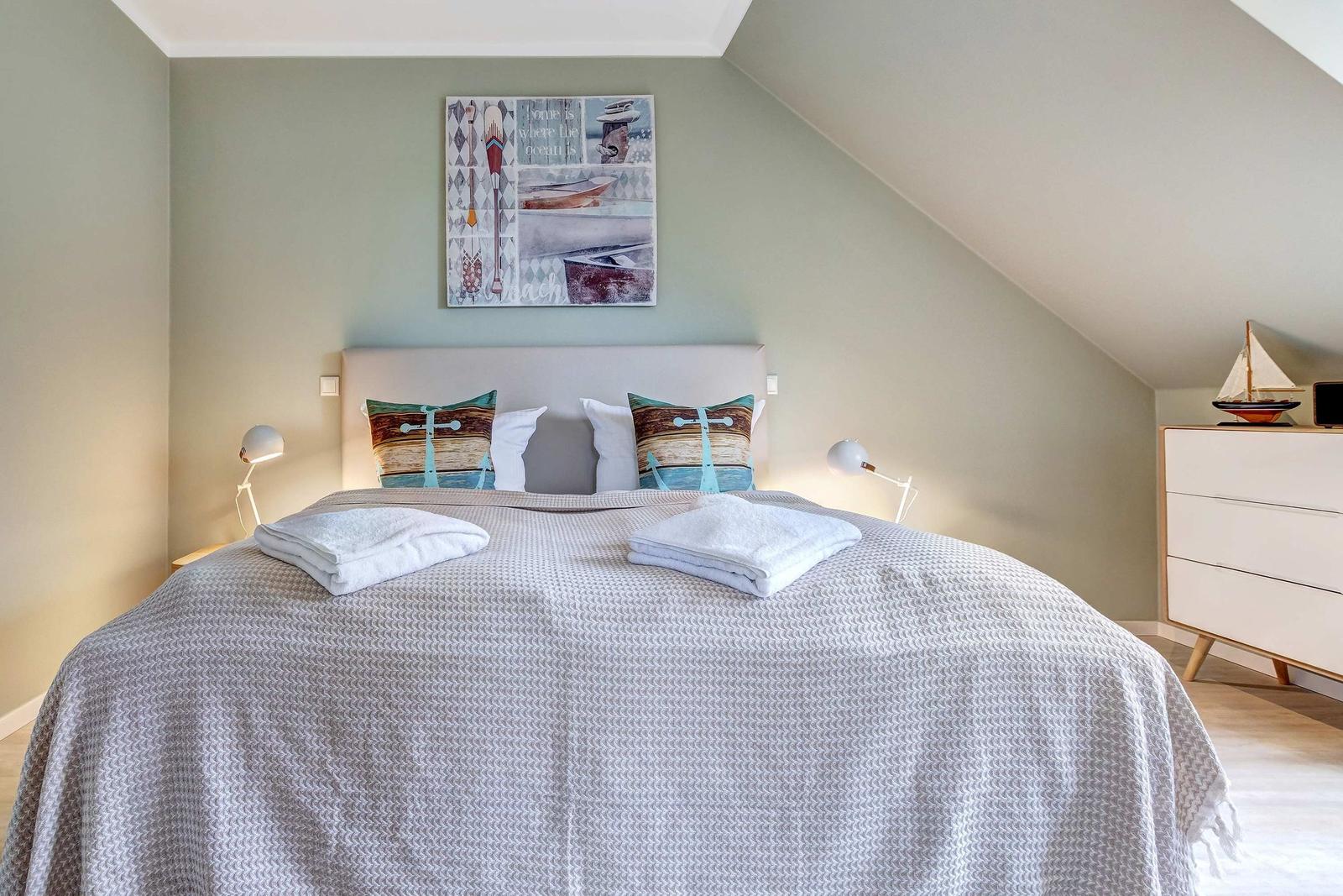 Schlafzimmer mit Bett, Wandbild und Schrank unter Dachschräge.