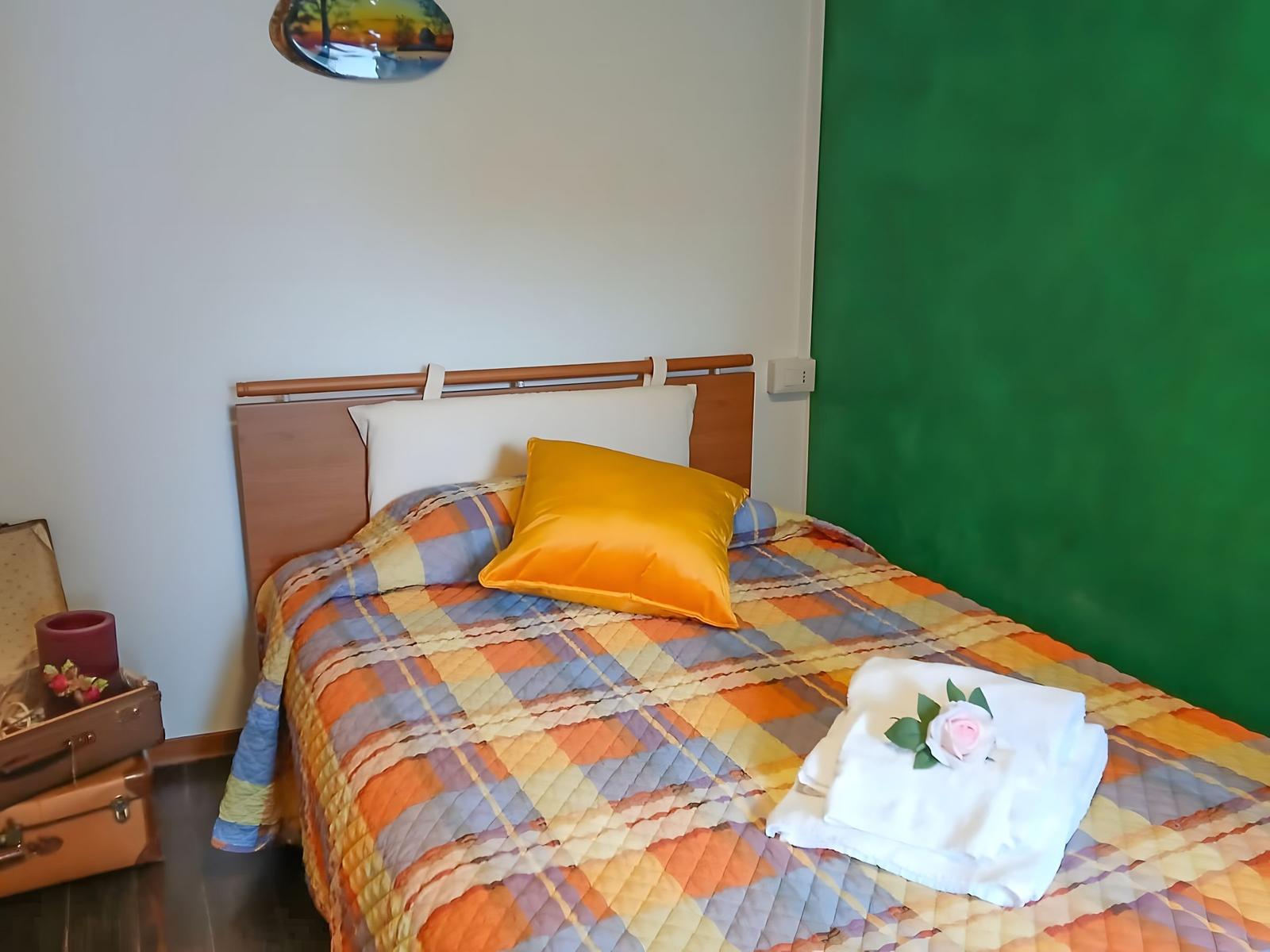 Ein Bett mit buntem Quilt, gelber Kissen und gefaltetem Handtuch mit Rose.