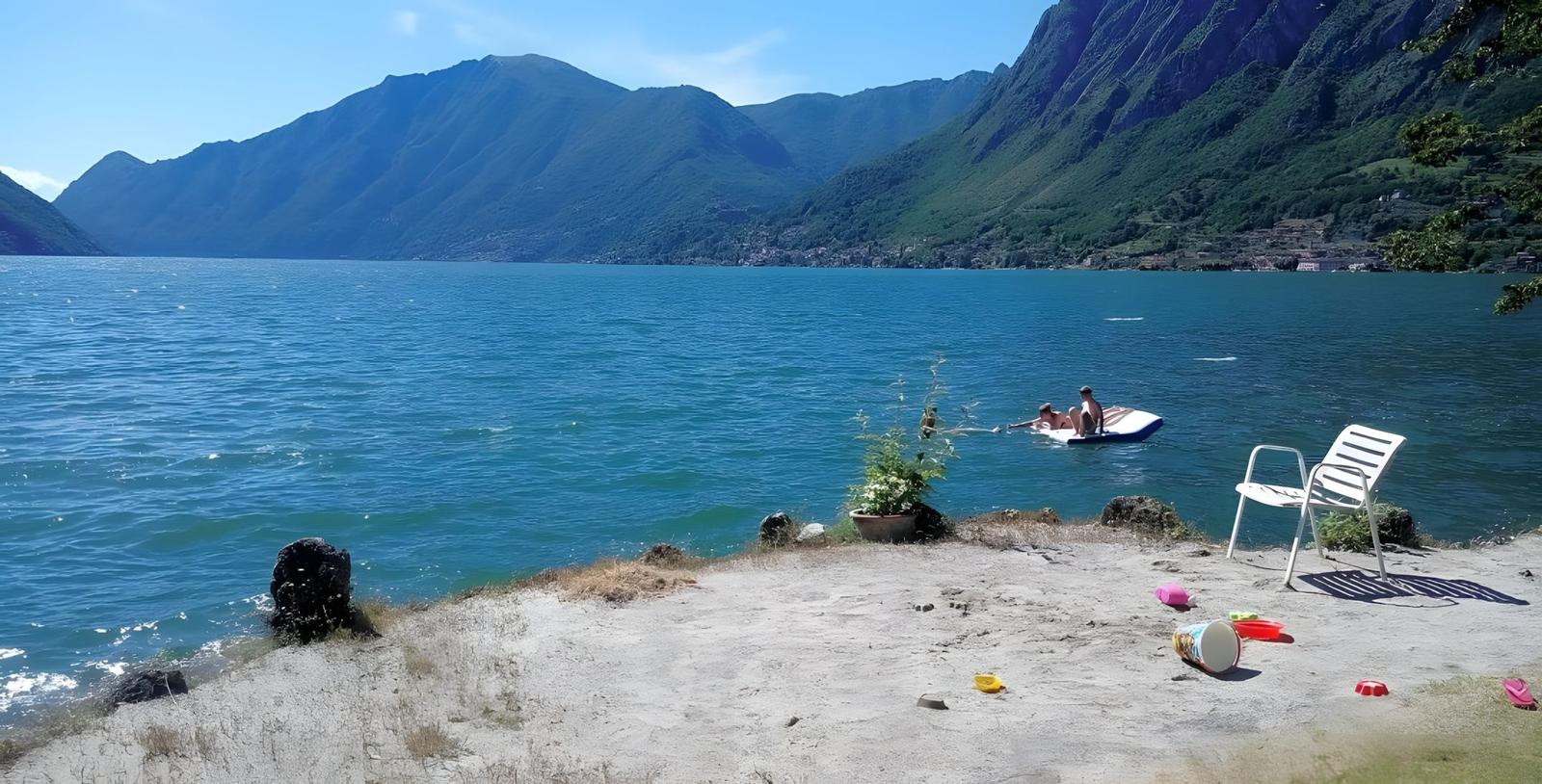 Lakeside with people on a float, white chair, and scattered toys on the shore.