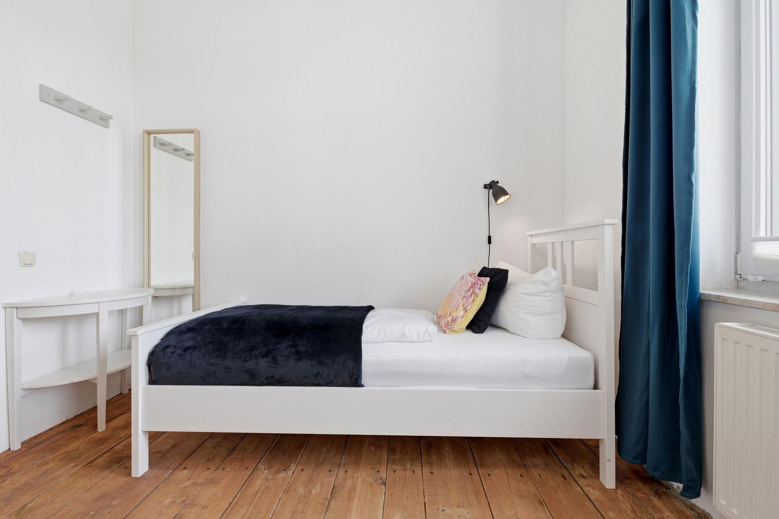 A bedroom with a white bed, wooden floor, and blue curtains.