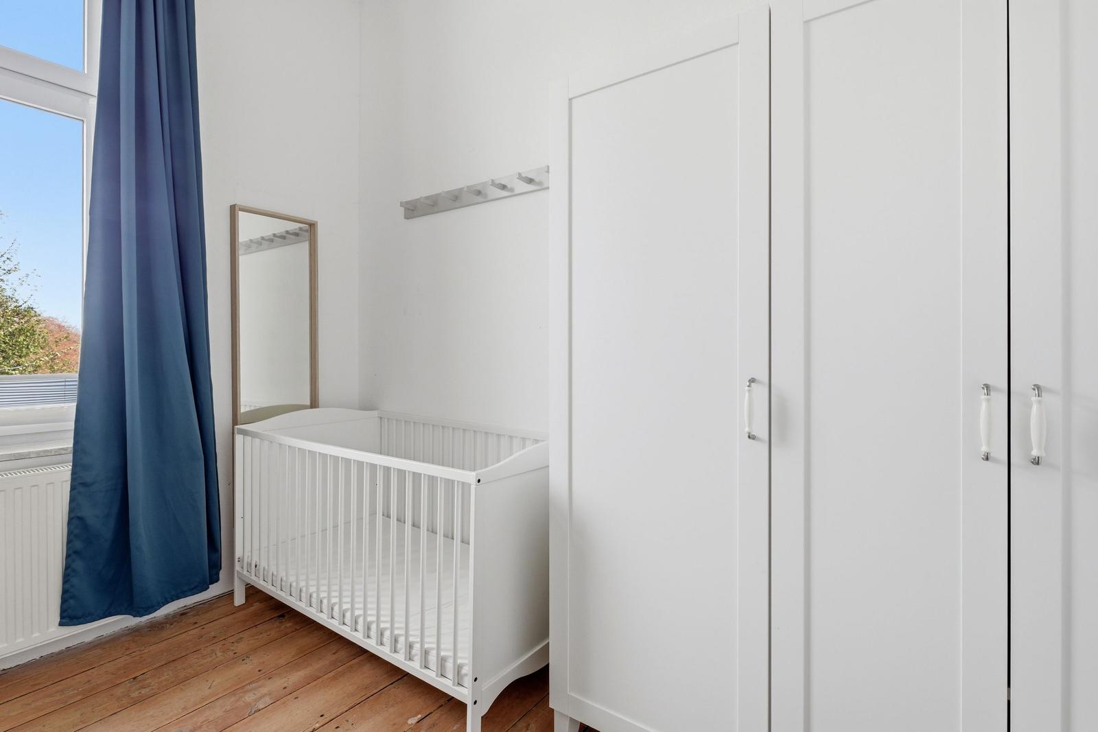 A room with a white crib, a mirror, and a white wardrobe.
