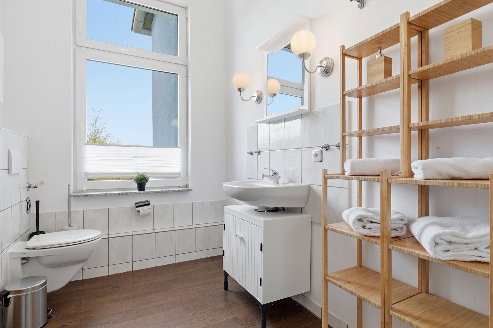 Bathroom with toilet, sink, and wooden shelf with towels.