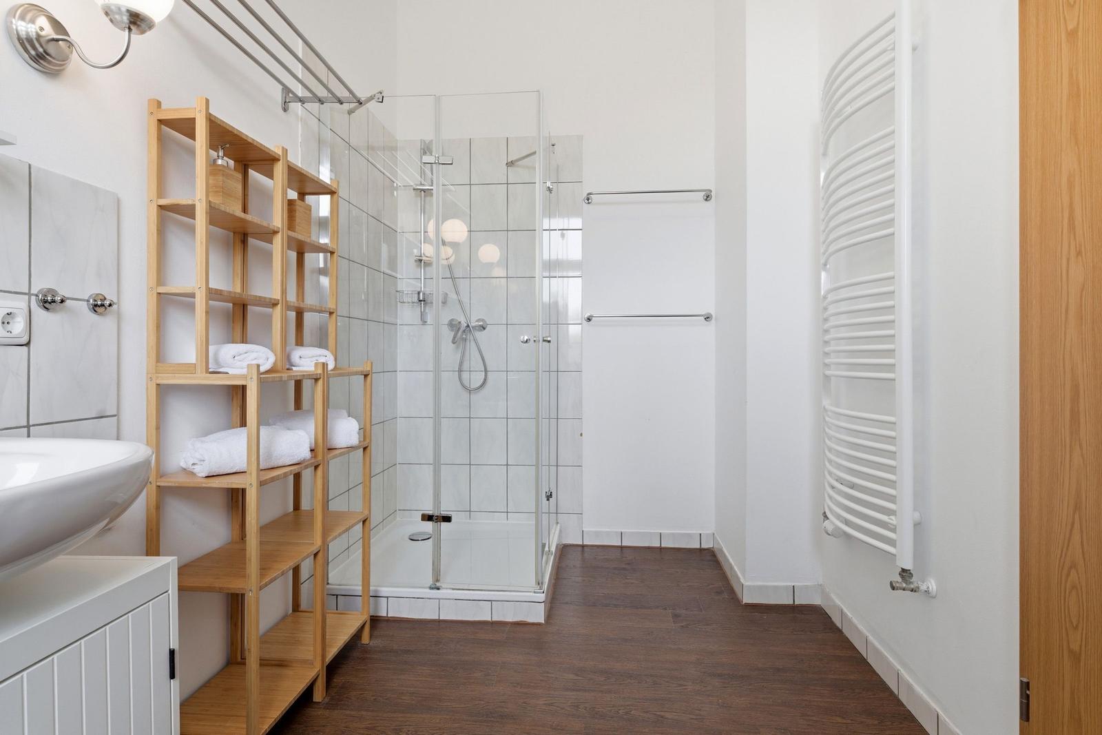 Bathroom with shower, sink, and wooden shelf.