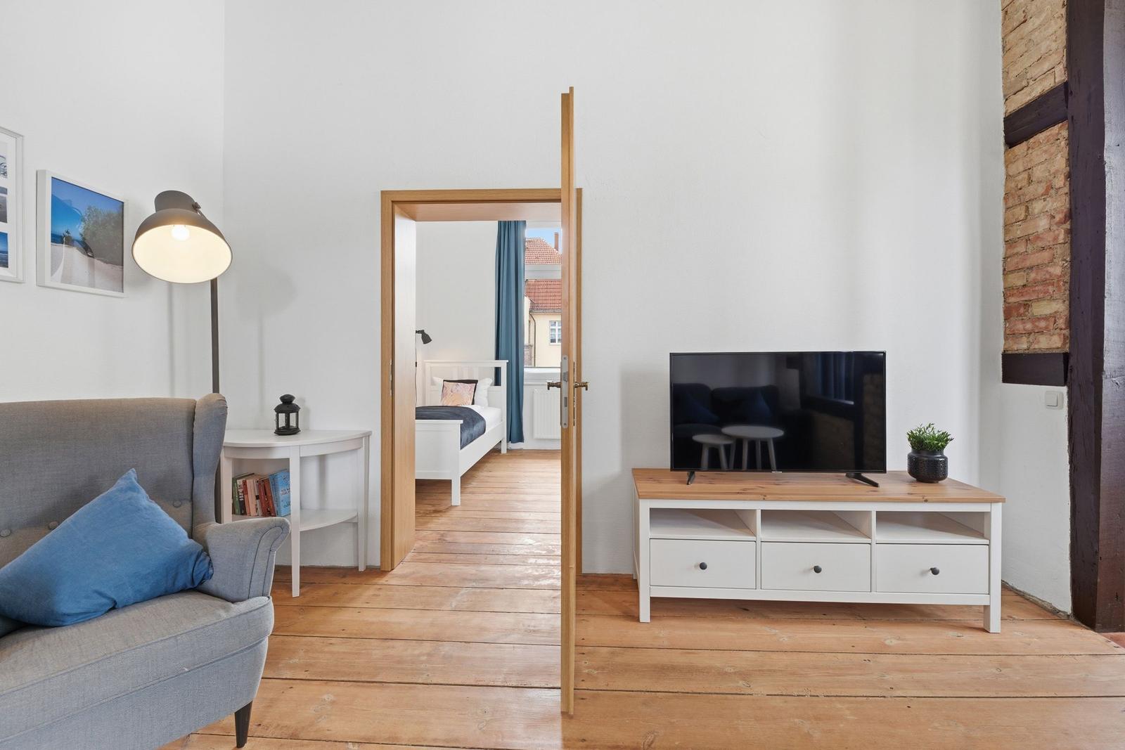 Living room with sofa, TV, and view into the bedroom.