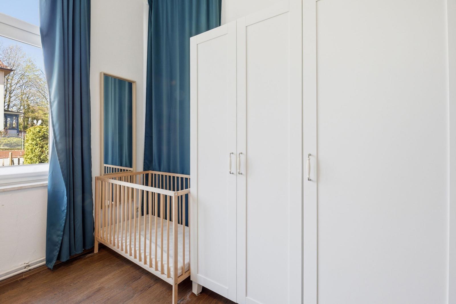 Childs room with crib, white wardrobes, and blue curtains.