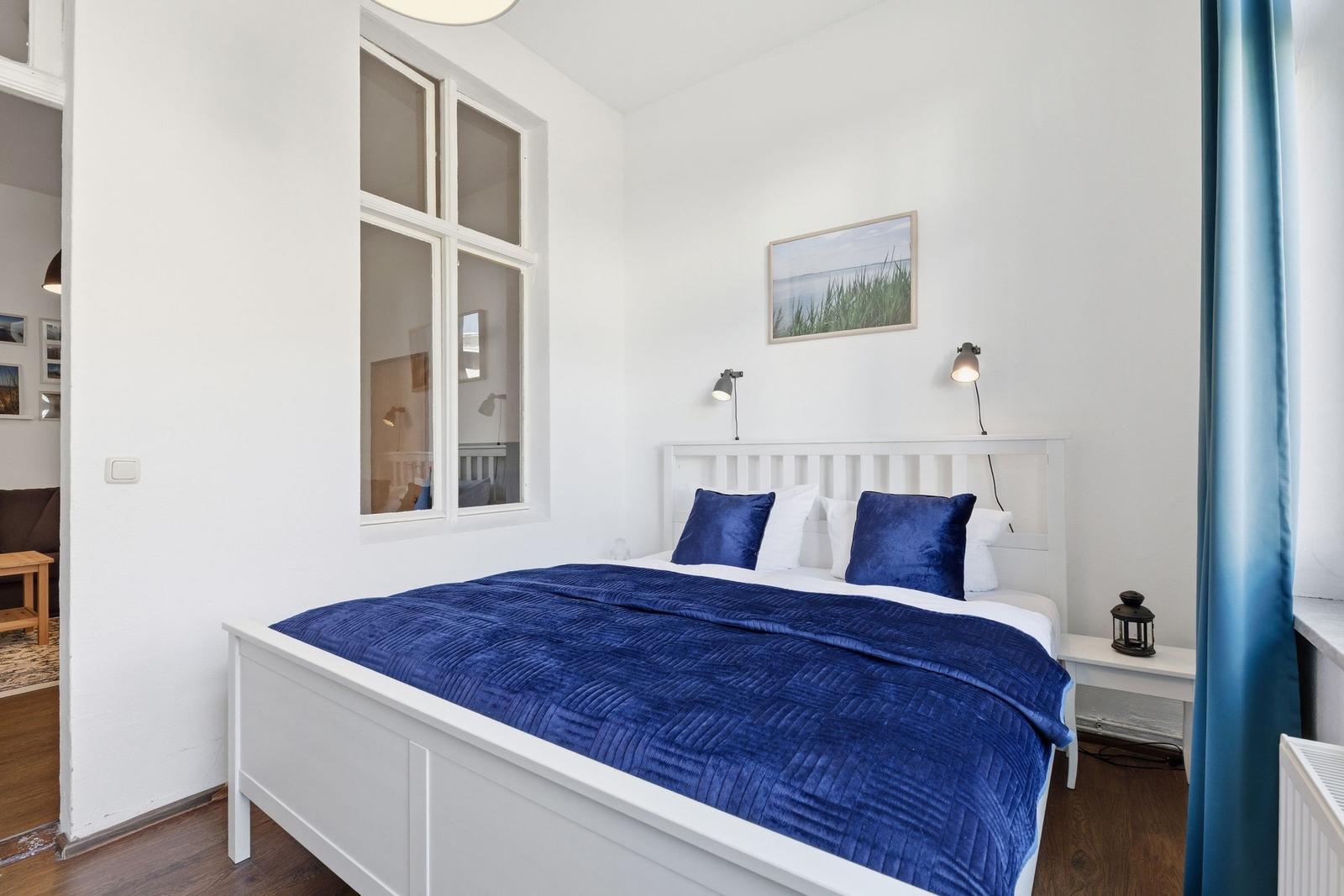 A bedroom with a white bed, blue bedding, and a window.