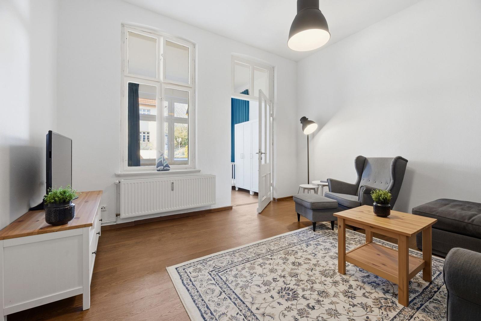 Living room with wooden floor, window, armchair, sofa, table, and rug.