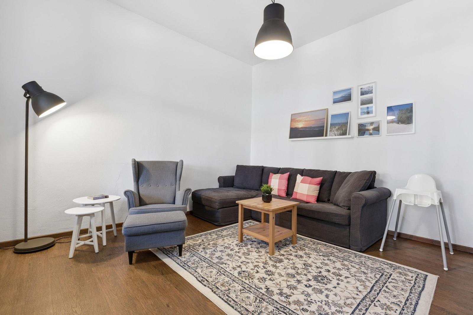 Living room with sofa, armchair, table, and rug. Wall art and floor lamp.