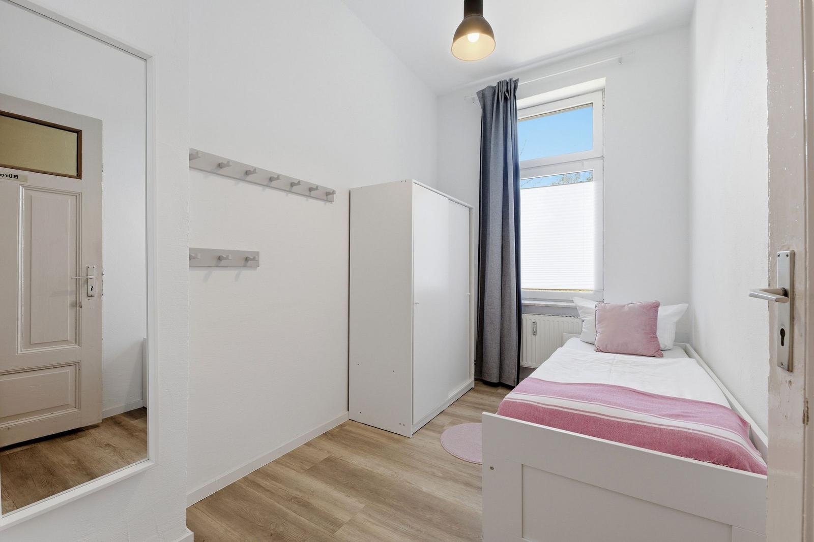 Ein Schlafzimmer mit Bett, Kleiderständer und Fenster.