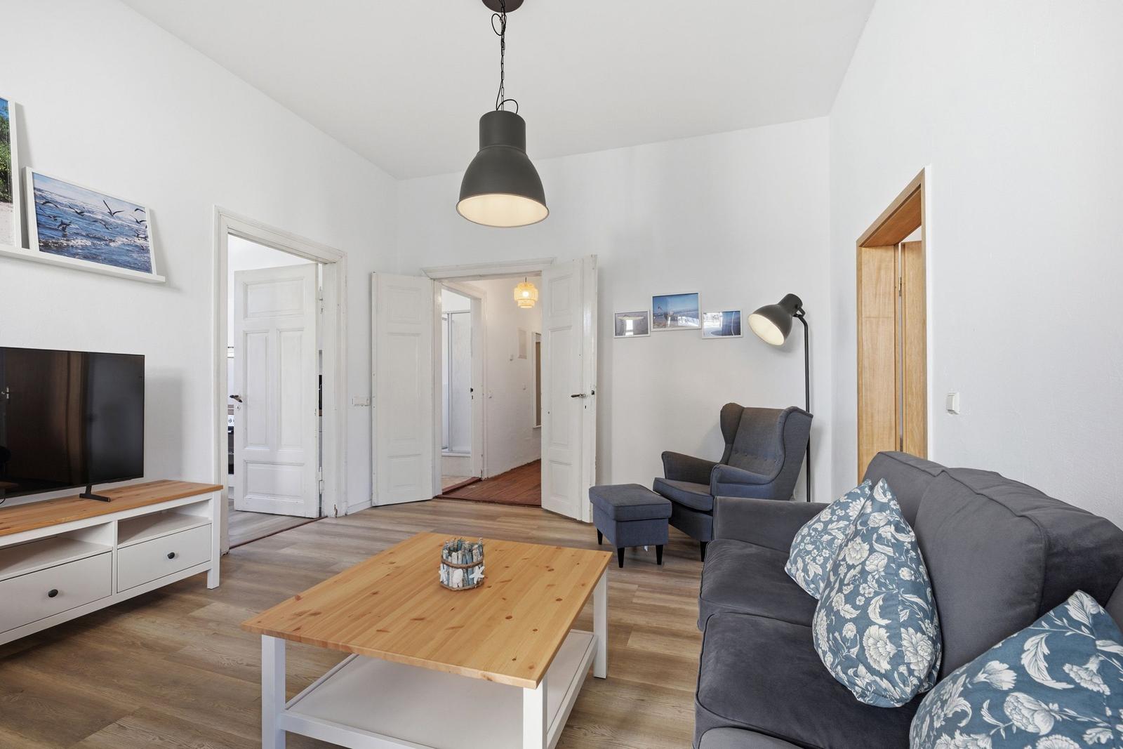 Wohnzimmer mit Sofa, Couchtisch und Fernseher. Helle Wände und Holzboden.
