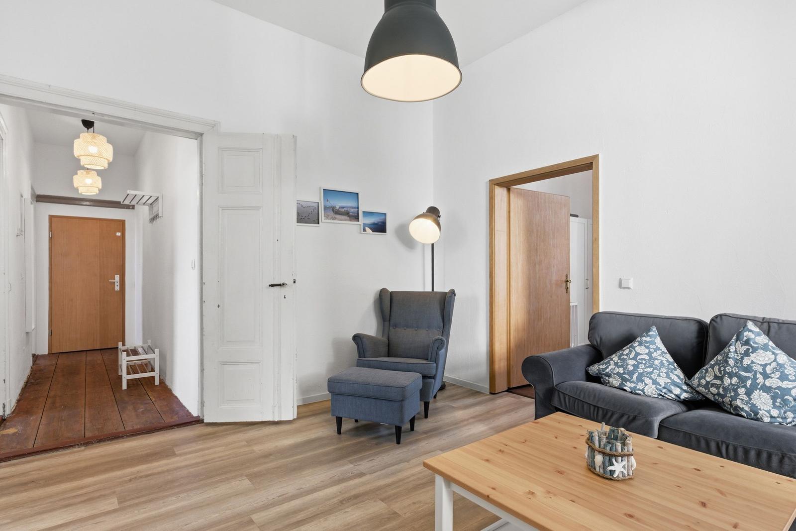 Wohnzimmer mit Sofa, Sessel, Tisch und Deckenbeleuchtung. Holzboden und weiße Wände.