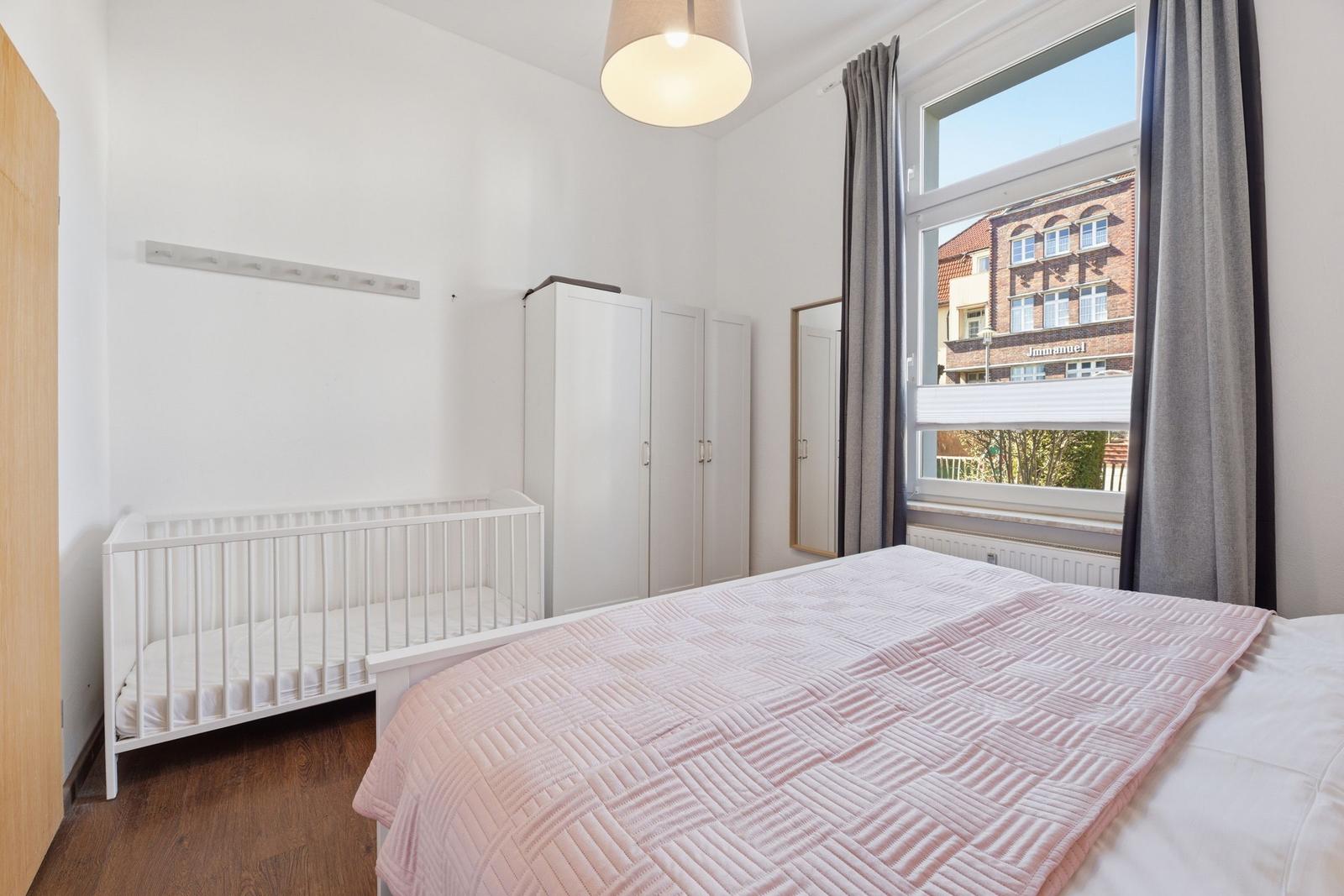 Schlafzimmer mit Bett, Kinderbett und Kleiderschrank. Blick auf Gebäude durch Fenster.