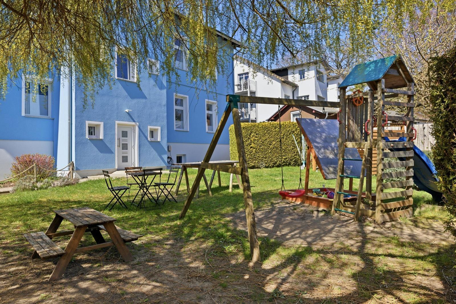 Backyard with playground, picnic table, and seating area under trees.