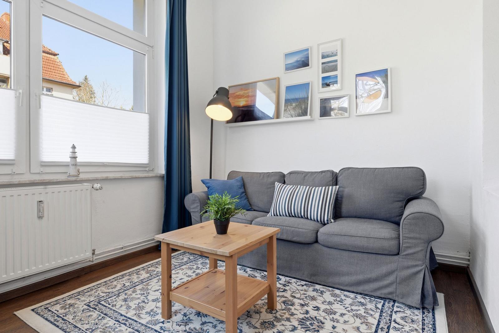 A living room with a gray sofa, wooden table, and window overlooking a house.