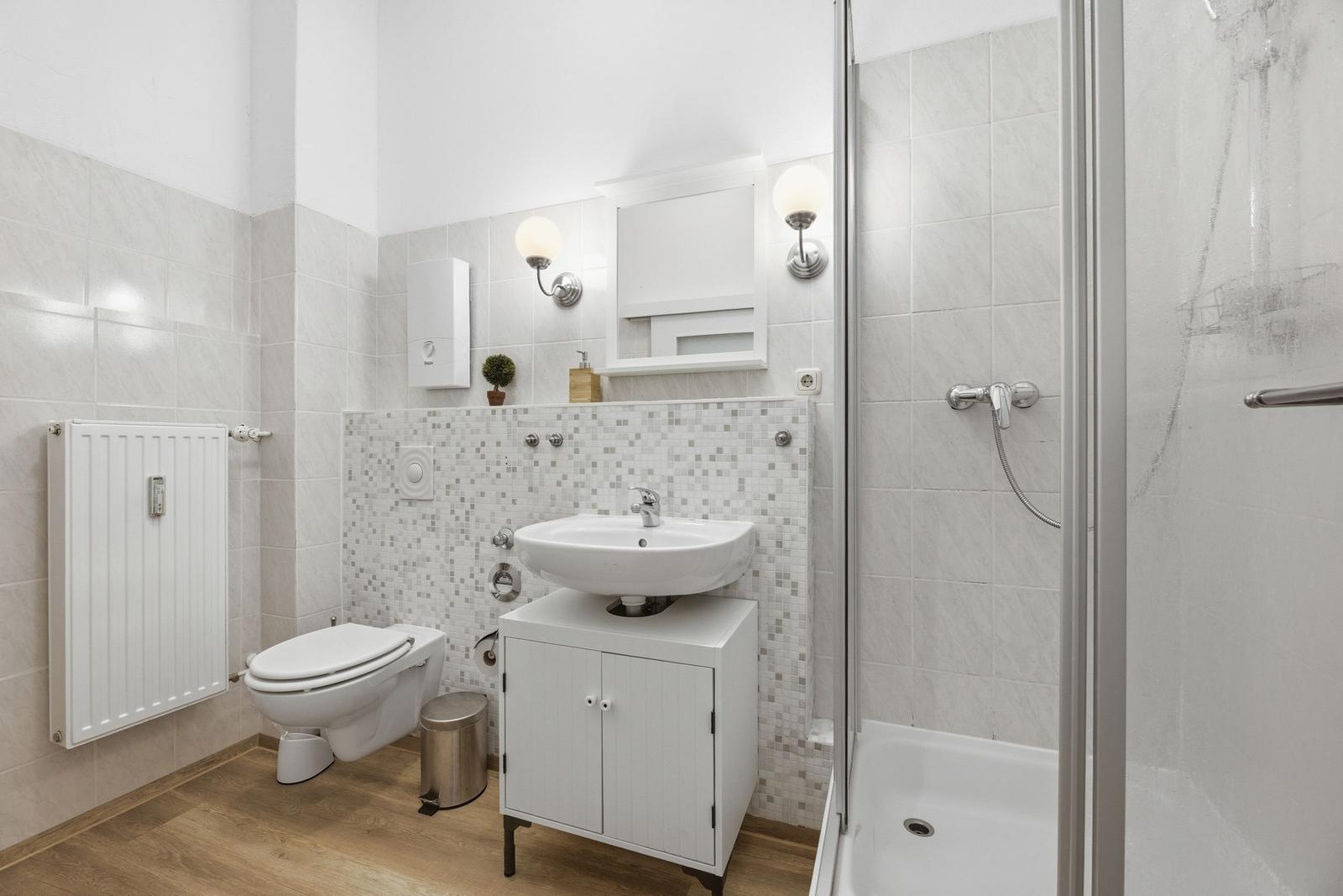 Badezimmer mit Dusche, Waschbecken und Toilette. Fliesenwand und Holzboden.