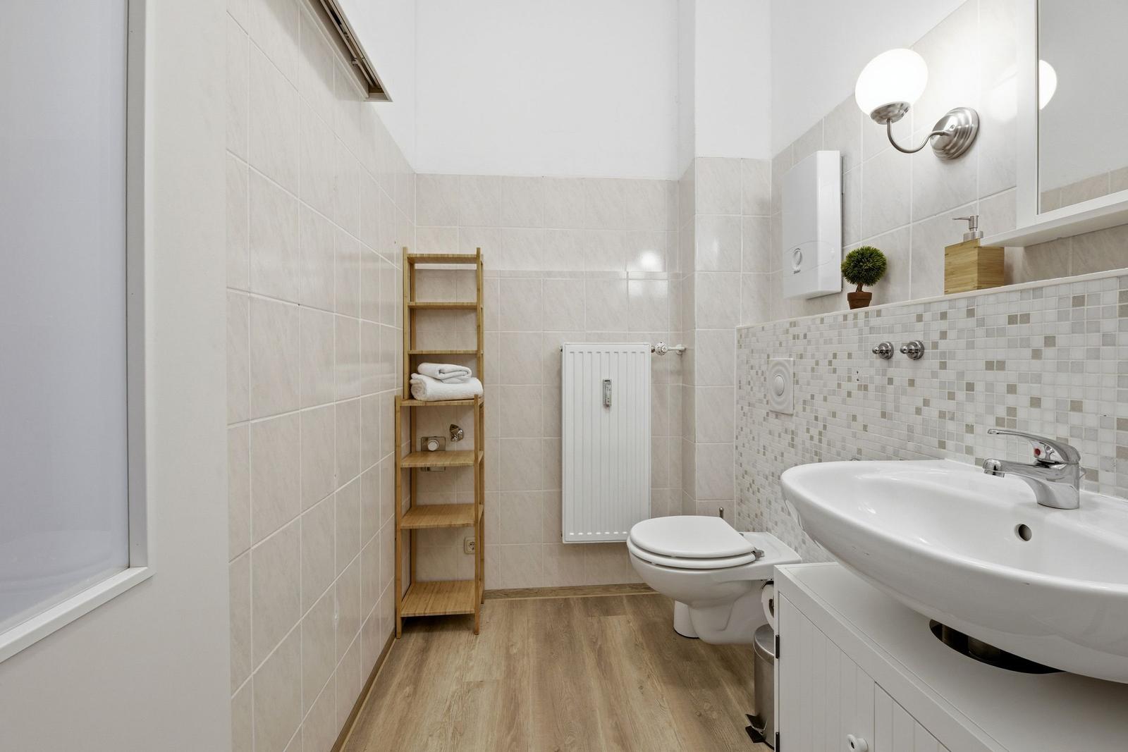 Badezimmer mit Toilette, Waschbecken und Holzregal an der Wand.