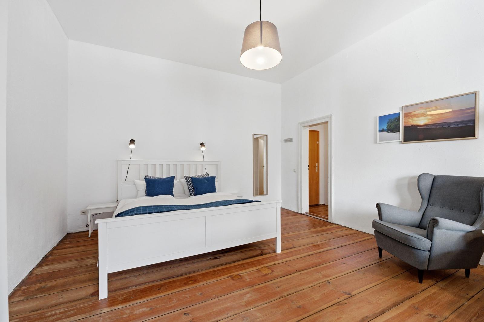 Schlafzimmer mit weißem Bett, Holzboden und grauer Sessel.
