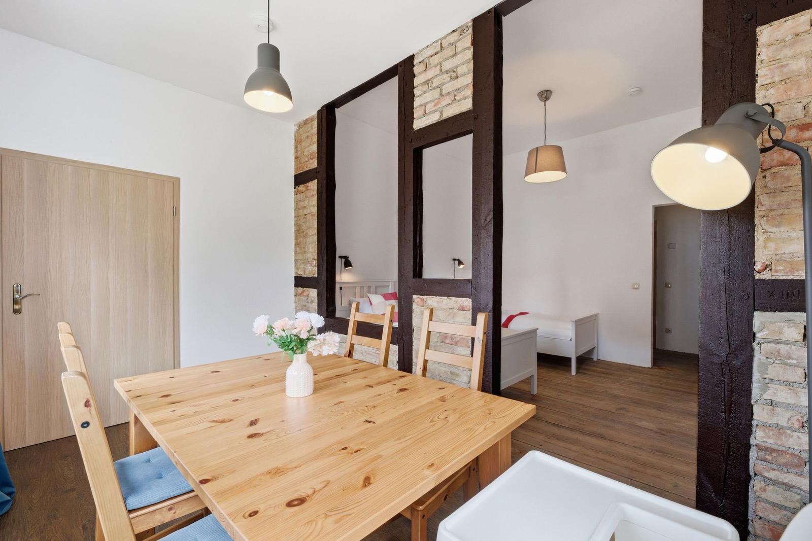Esszimmer mit Holztisch und Stühlen, Blick in Schlafzimmer mit Bett und Holzbalken.