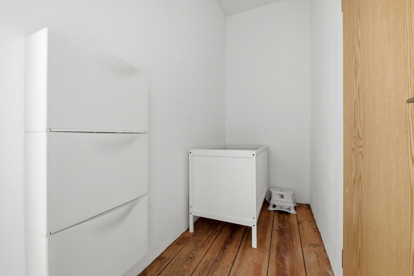 Ein Raum mit weißem Schrank, weißem Kinderbett und Holzboden.