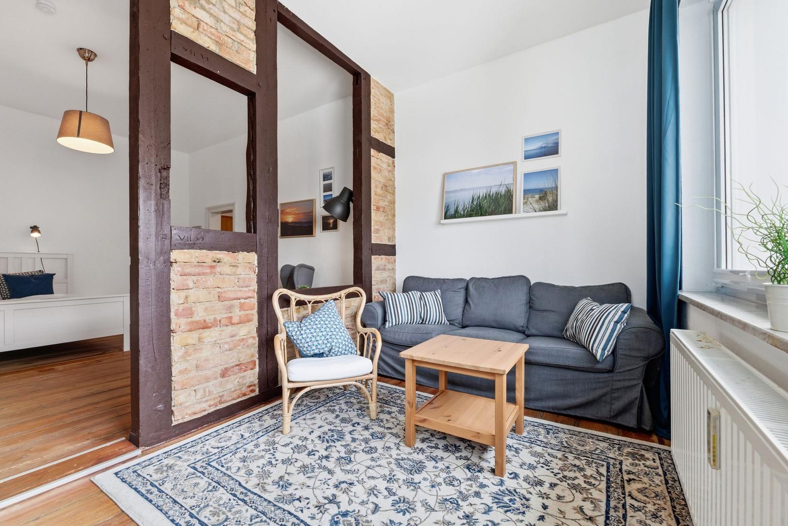 Wohnzimmer mit Sofa, Stuhl und Teppich. Holzfußboden und Fenster mit Vorhang.