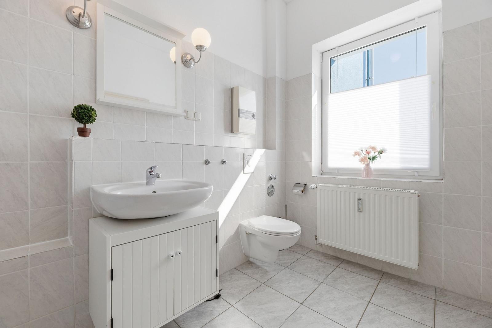 Bathroom with sink, toilet, and window with flowers.