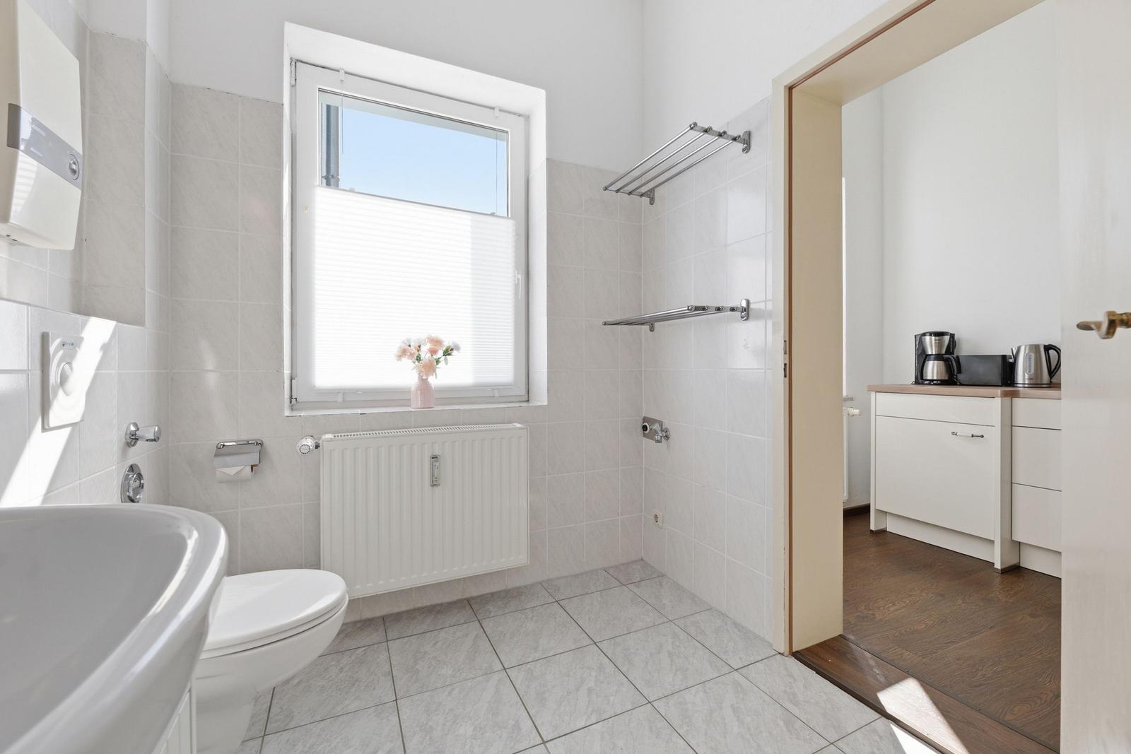 Bathroom with toilet, sink, and window. Passage to kitchen with worktop.