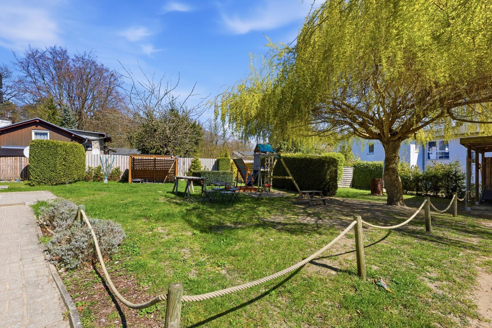 Backyard with playground, table, chairs, and large tree.