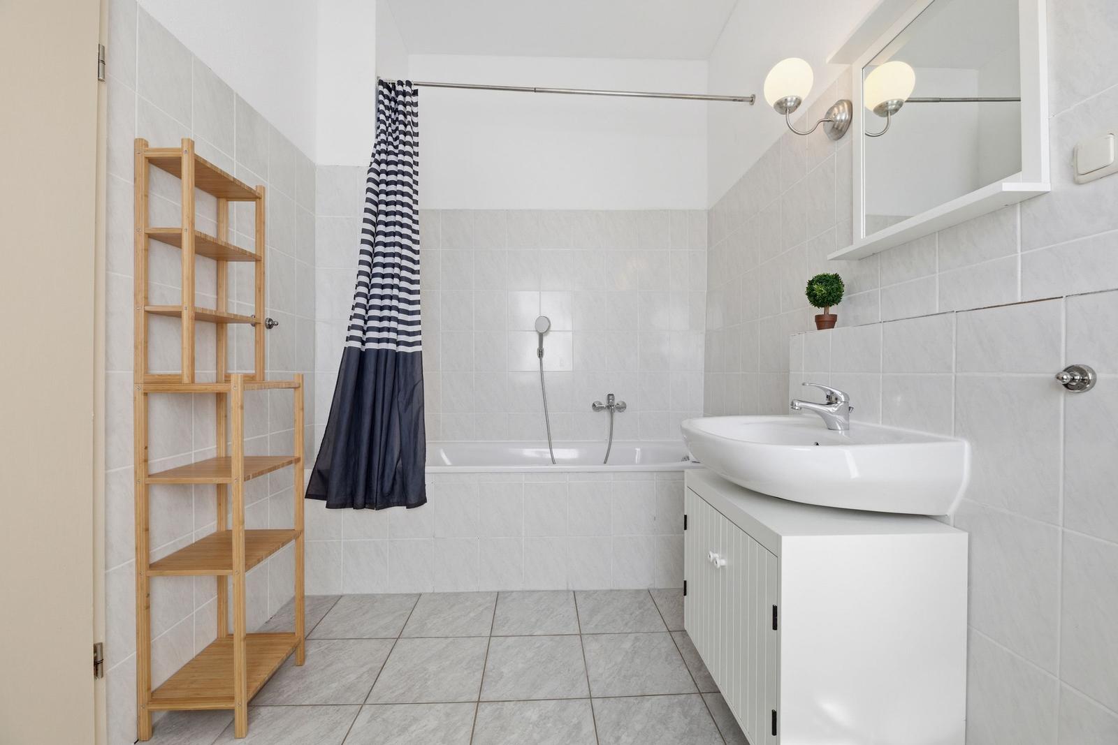 Bathroom with bathtub, sink, and wooden shelf.