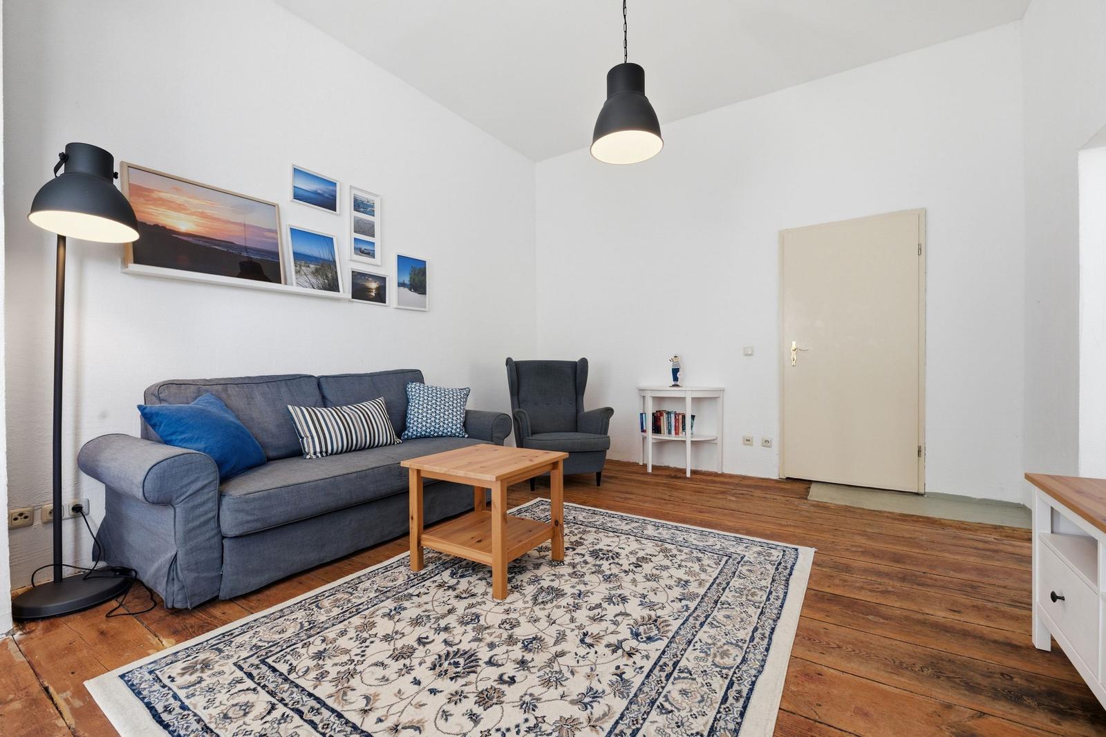 Living room with sofa, armchair, table, and rug on wooden floor.