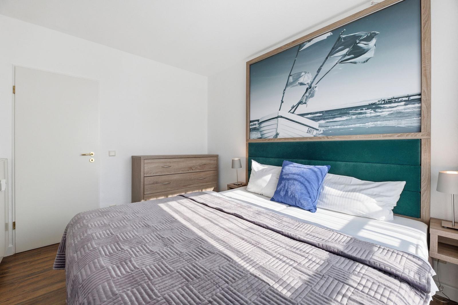 Schlafzimmer mit Bett, Kopfteil und Wandbild eines Segelboots.