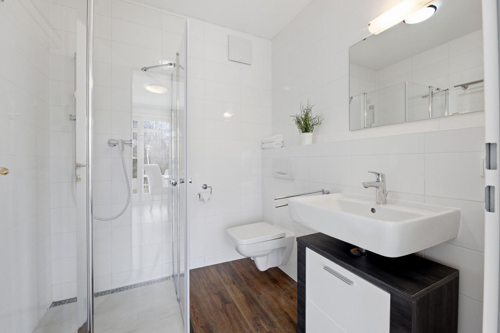 Badezimmer mit Dusche, Waschbecken und Toilette. Fliesenwand und Holzboden.