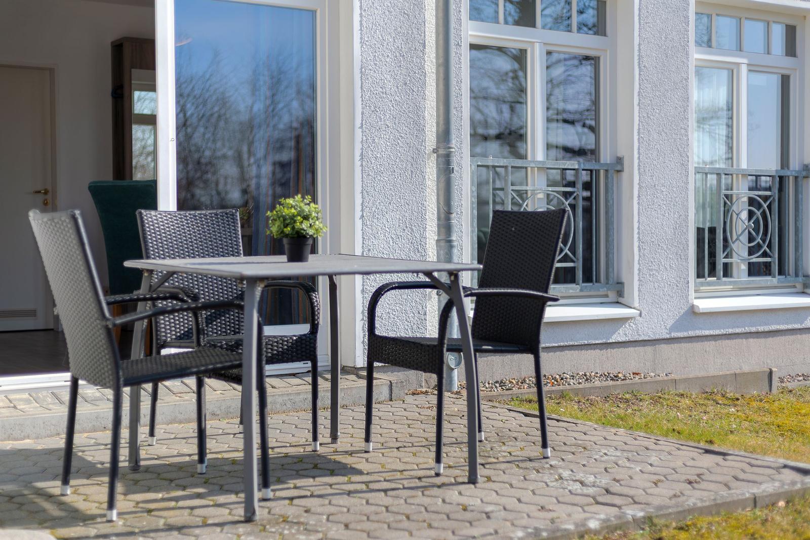Terrasse mit Tisch und Stühlen vor einem Haus mit Fenstern und Balkon.