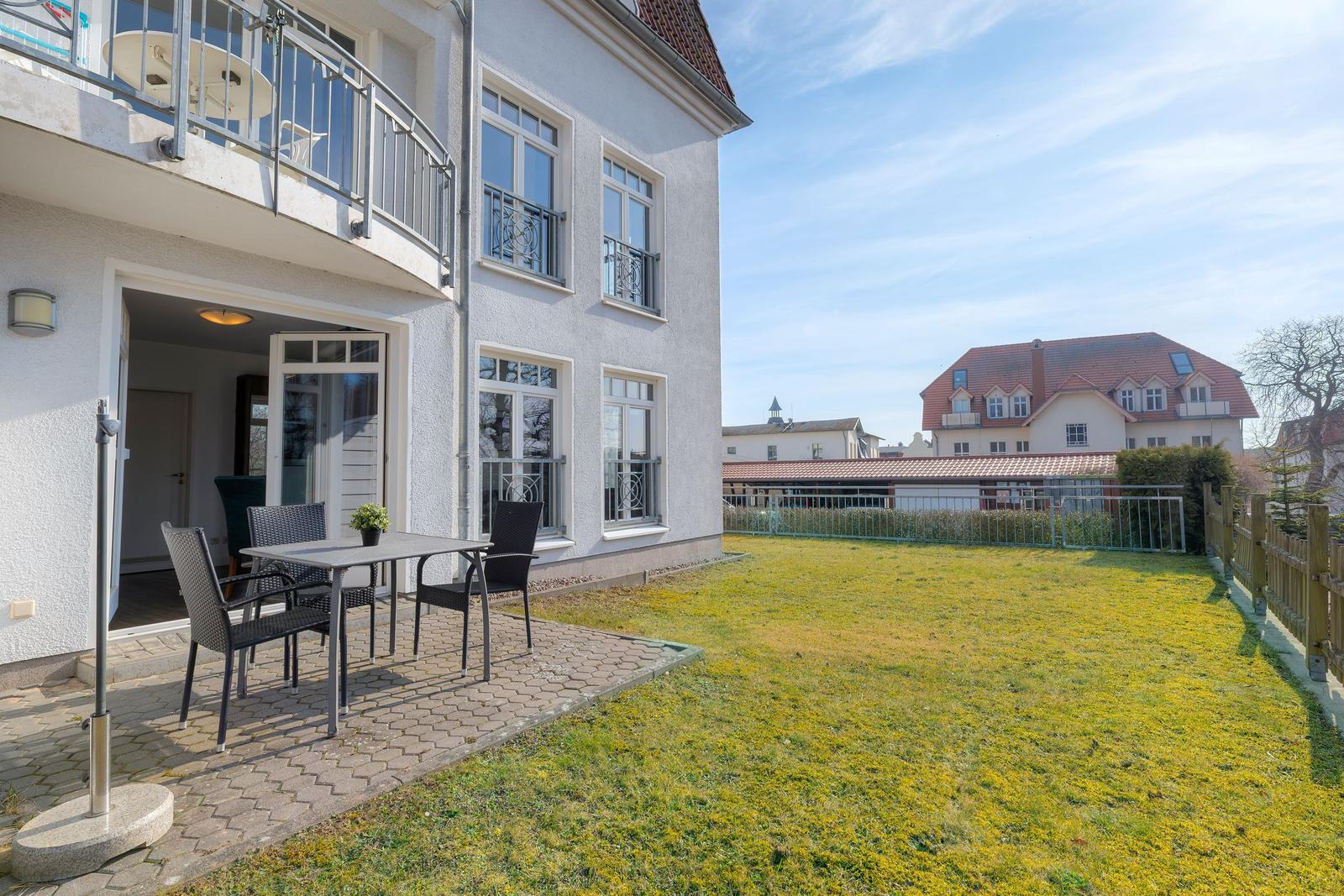 Haus mit Balkon, Terrasse und Garten. Im Hintergrund sind weitere Gebäude zu sehen.