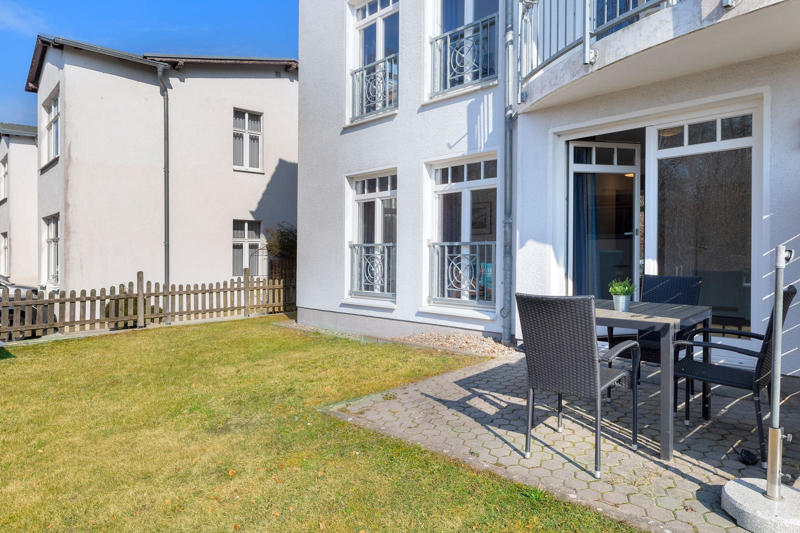 Hinterhof mit Garten, Terrasse und Sitzgelegenheiten. Haus mit Balkon und Fenstern.