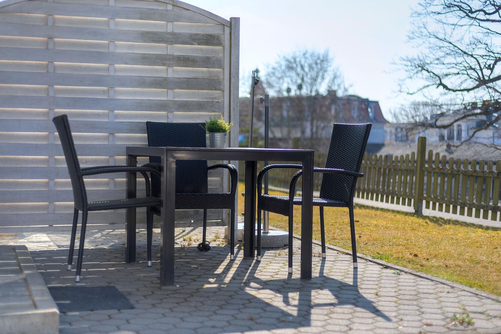 Außenbereich mit Tisch und drei Stühlen auf gepflastertem Boden.
