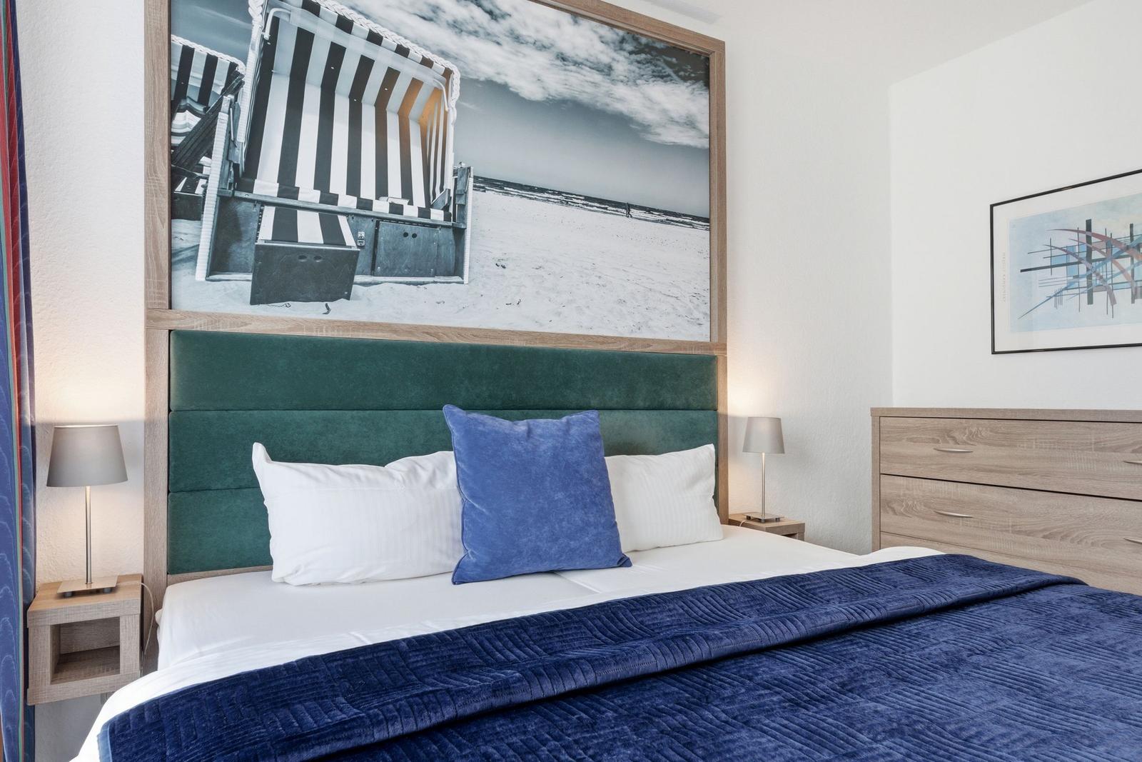 Schlafzimmer mit Bett, Nachttischen und Wandbildern.