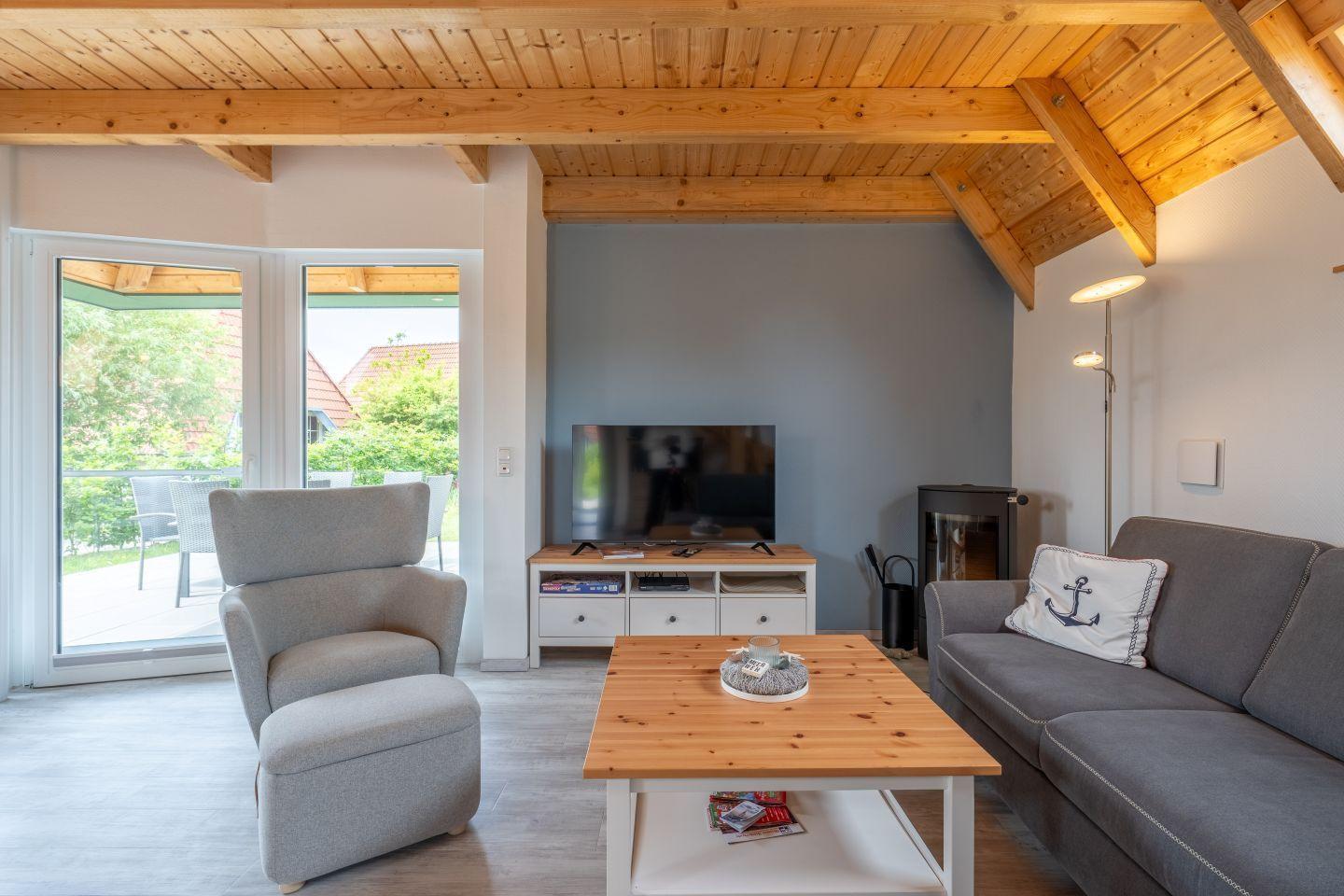Wohnzimmer mit Sofa, Sessel, Couchtisch und Fernseher. Holzdecke und Terrassentür.