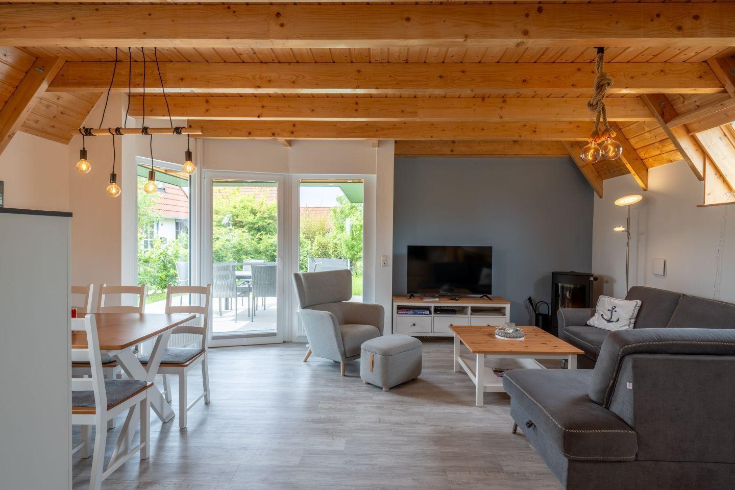 Wohn- und Essbereich mit Holzdecke, Sofa, Fernseher und Terrassenzugang.