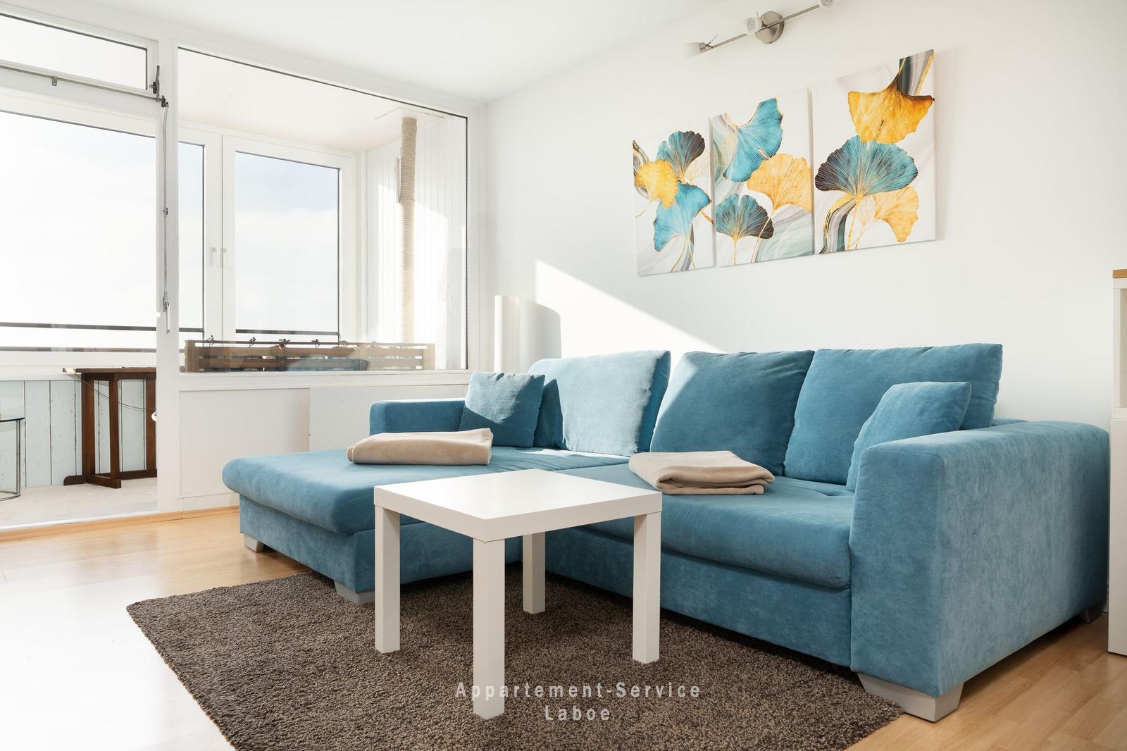 Ein Wohnzimmer mit blauem Sofa, weißem Tisch und Wandbildern.