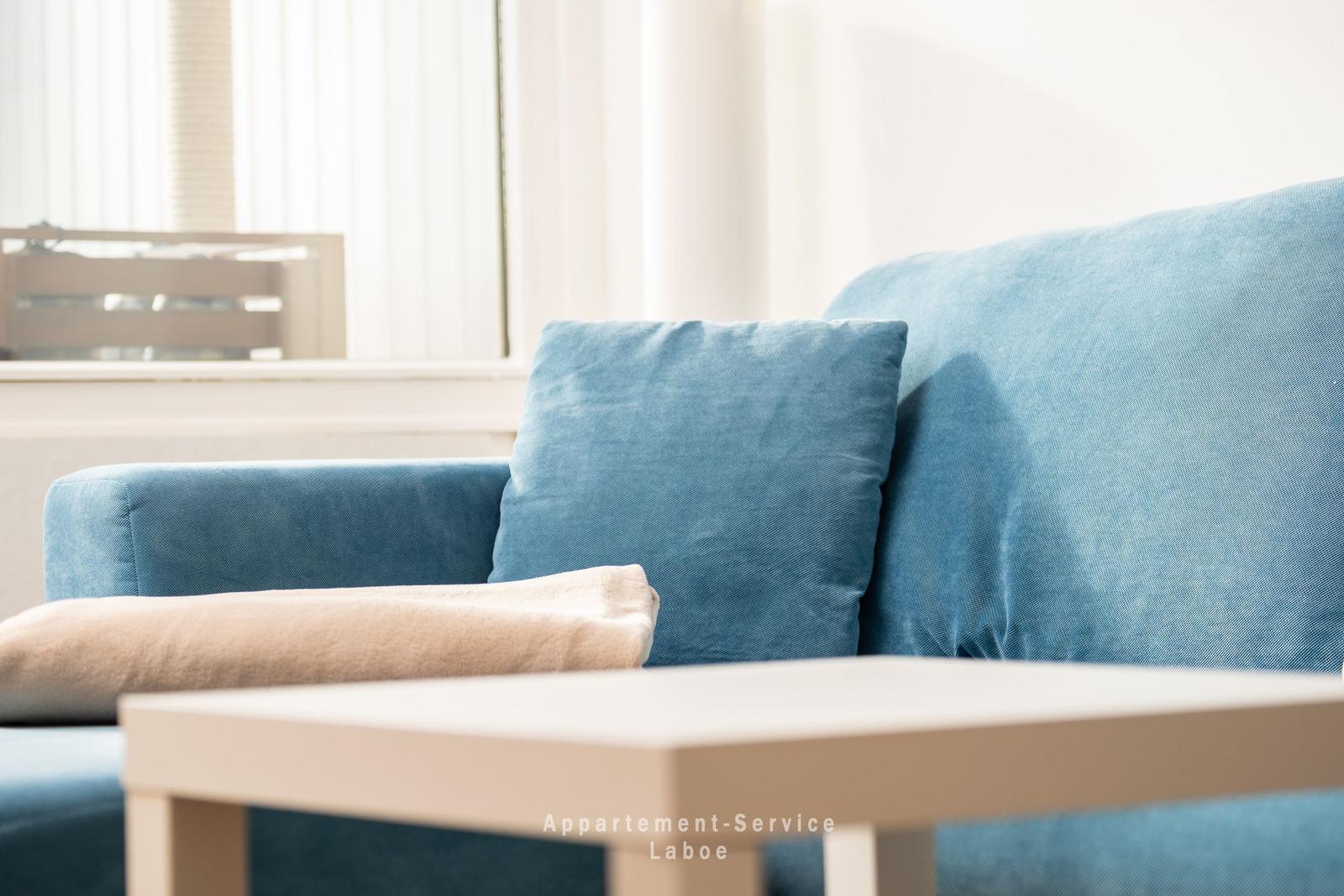 Blauer Sessel mit Kissen und Couchtisch vor Fenster