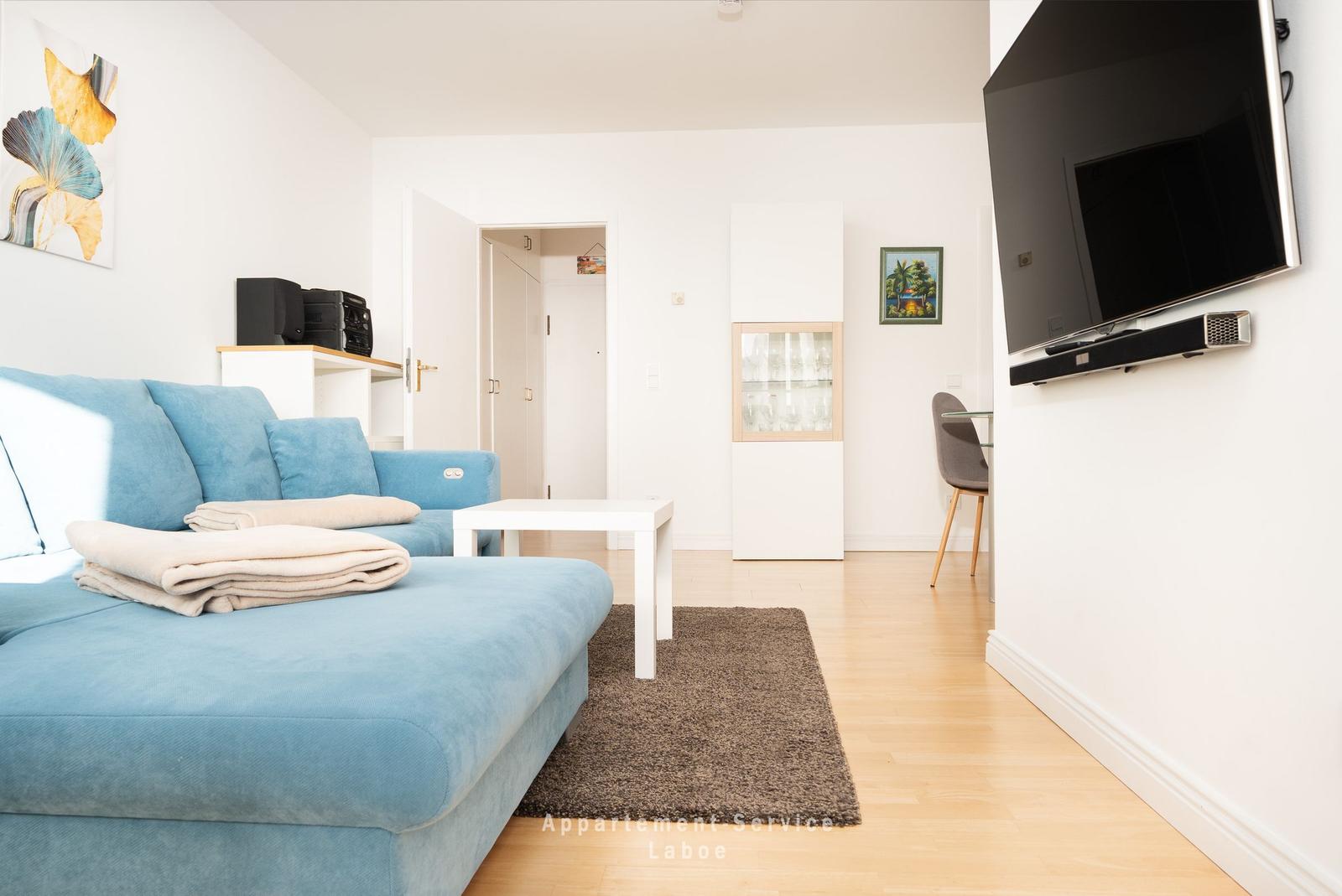 Ein Wohnzimmer mit blauem Sofa, Fernseher und Holzboden.