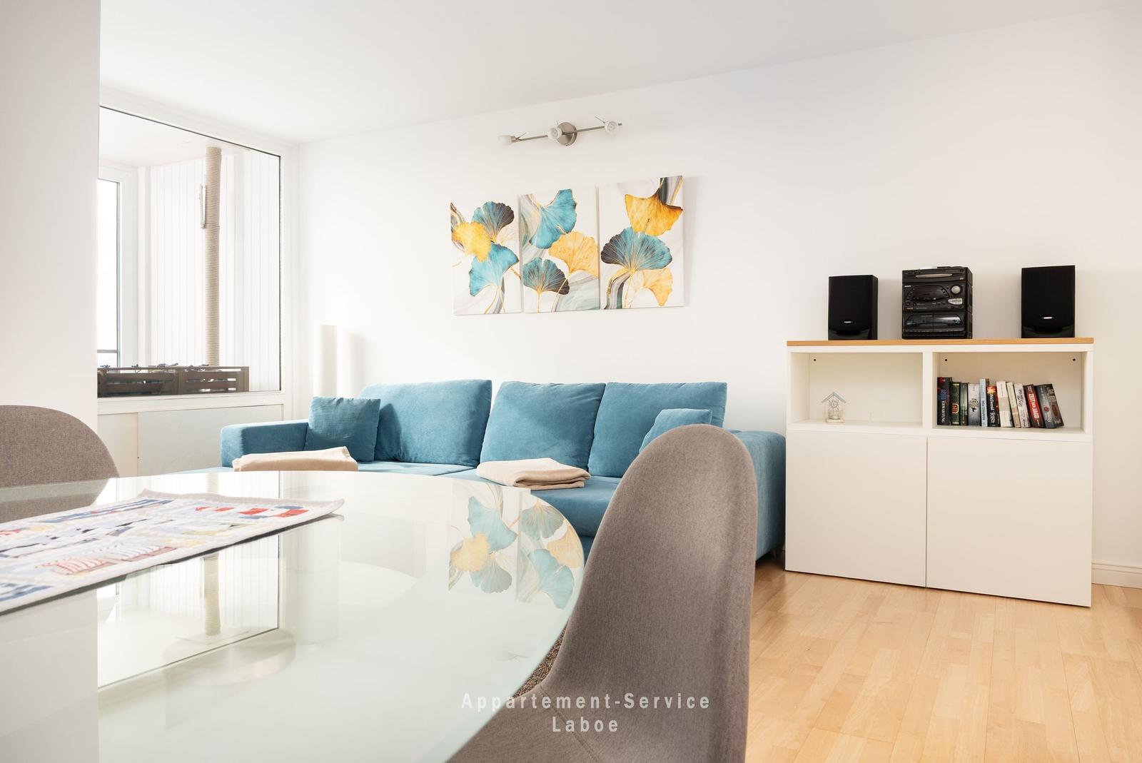 Blauer Sofa im Wohnzimmer mit Glas-Tisch und Wandbildern.