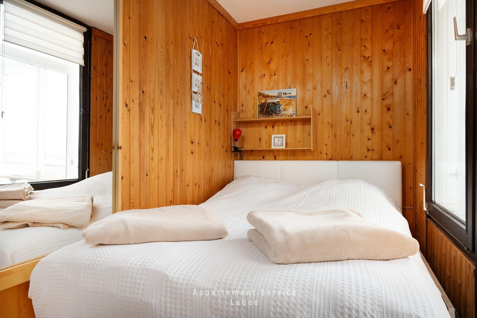 Schlafzimmer mit Holzwand, Bett und Fenster. Auf dem Bett liegen gefaltete Handtücher.